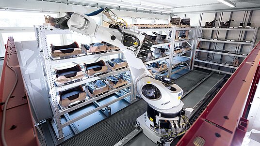 A view into the robot and workpiece magazine system RS3 with the additional linear axis, consisting of the robot with gripper and three (left) plus one (back) rack units making a total of 43 workpiece pallets